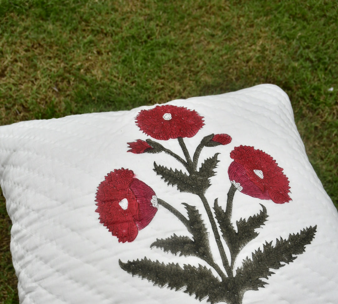 White pillow with red floral design on grass