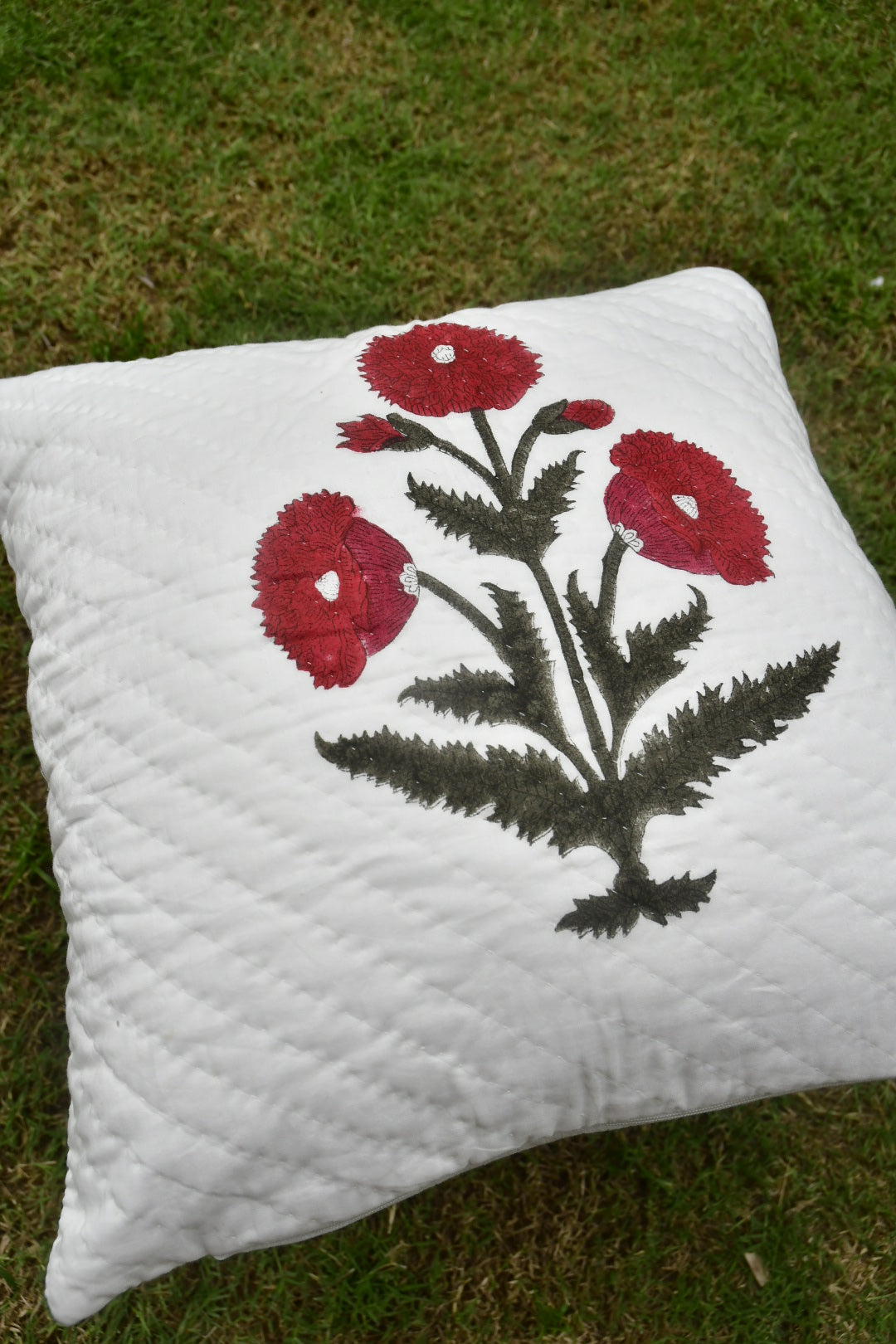 White pillow with red floral design on grass