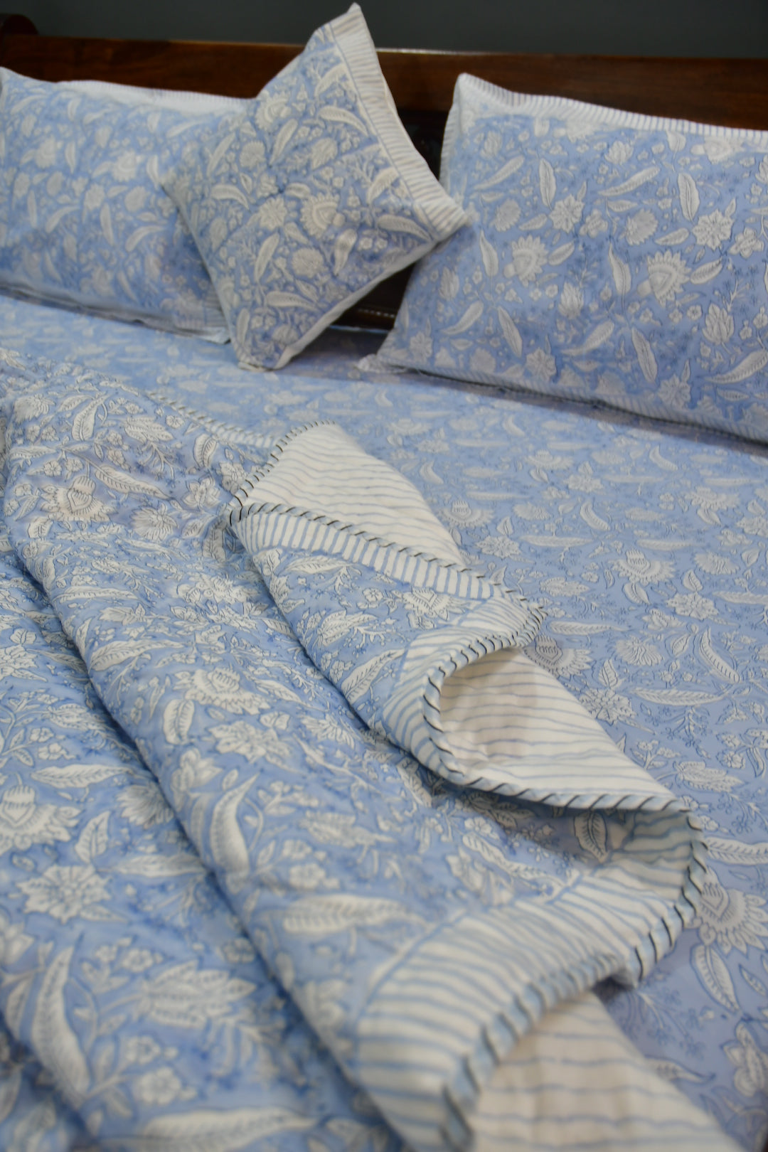 Blue and white patterned fabric with pillows and a blanket on a wooden surface
