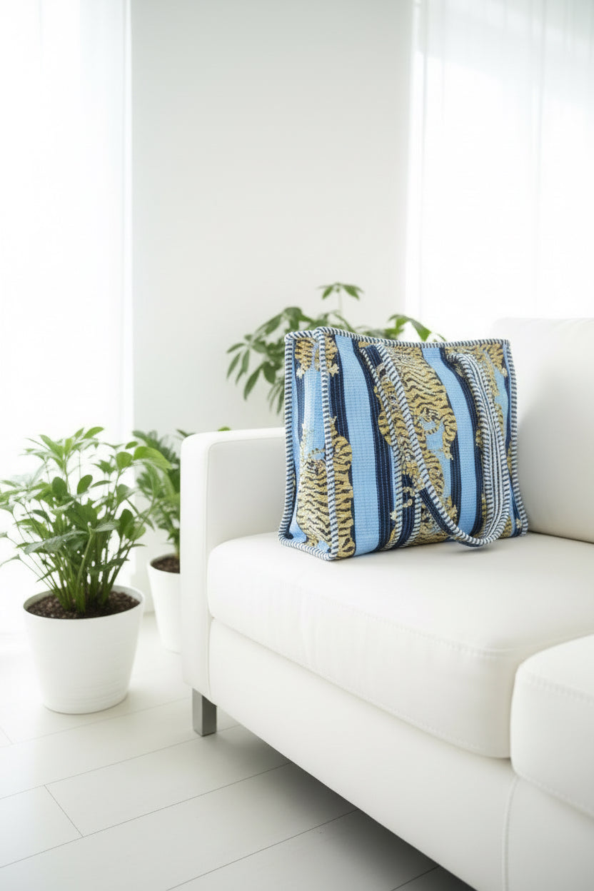 White sofa with a decorative pillow featuring blue and brown patterns, surrounded by potted plants in a bright room.