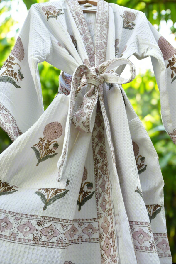White robe with floral patterns and a bow, hanging outdoors with greenery in the background