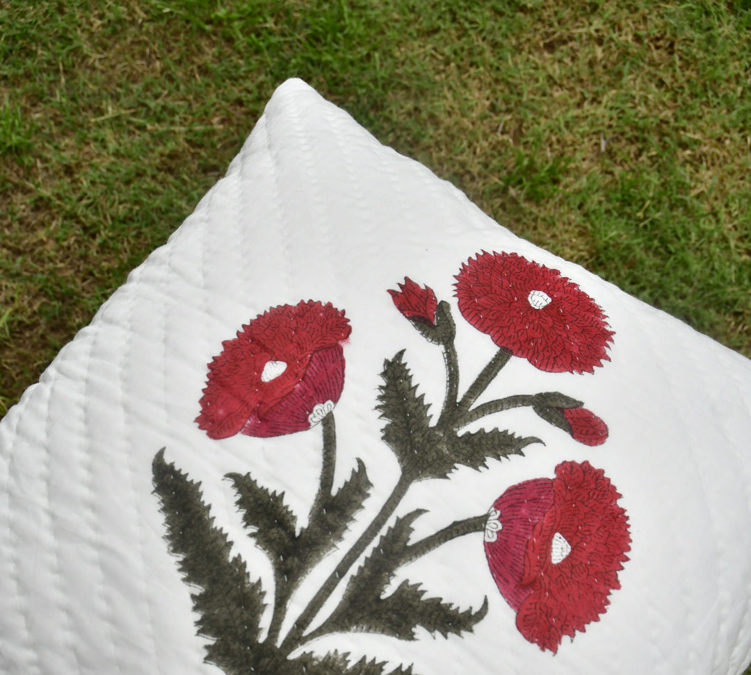White pillow with red floral embroidery on a grassy background