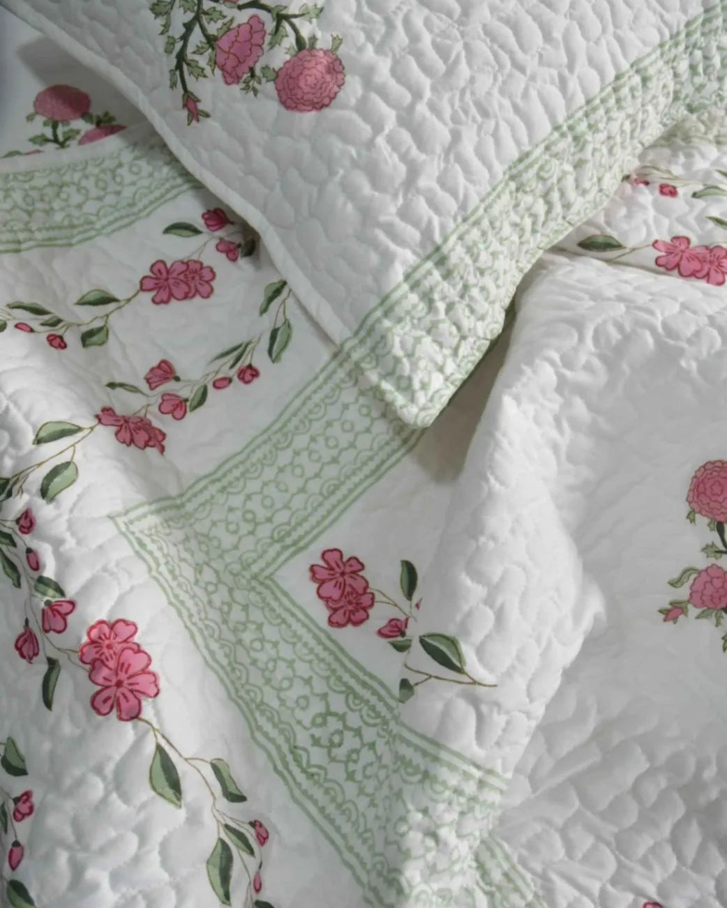 Floral quilt with pink flowers and green leaves on a white background