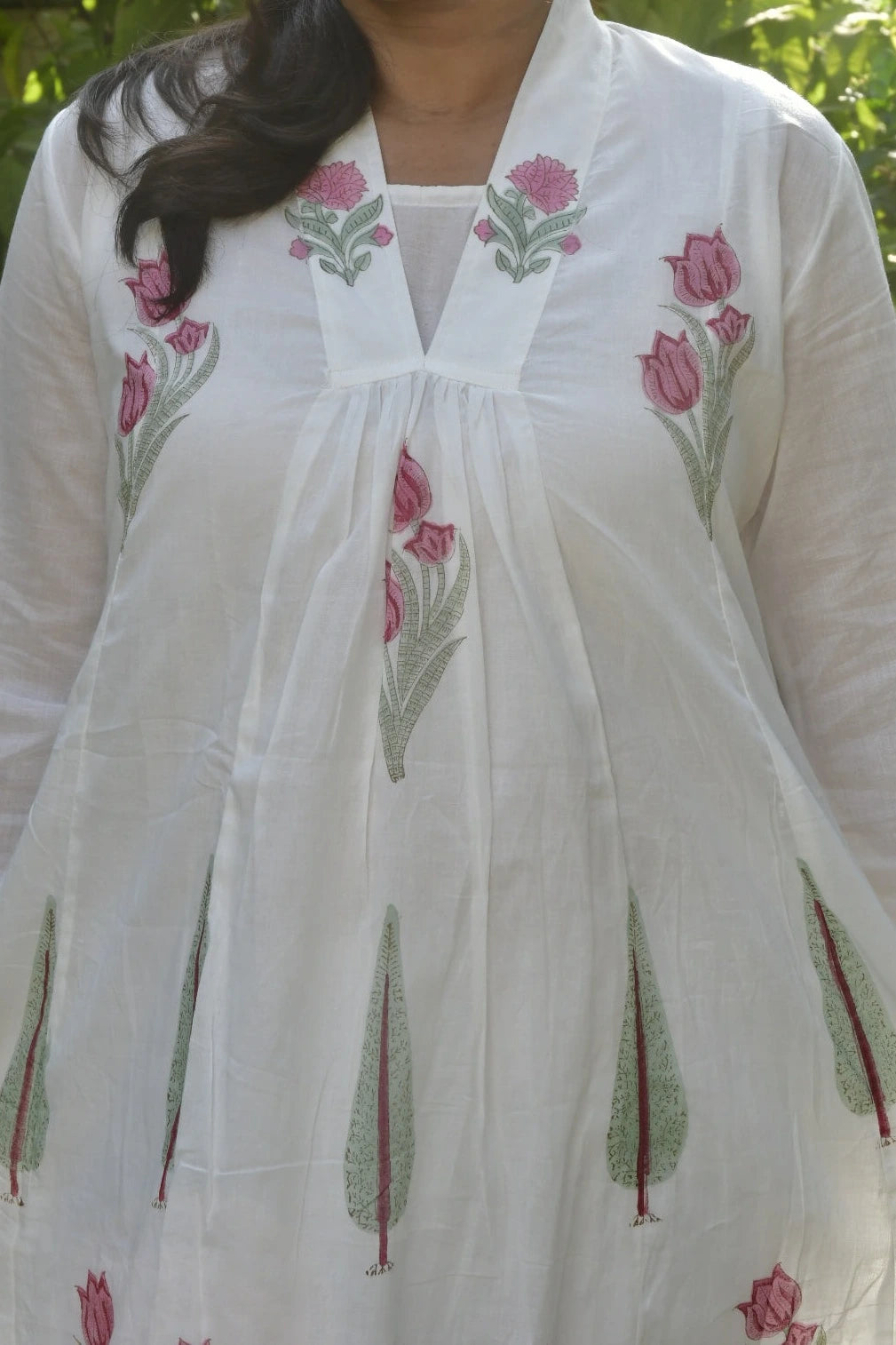 White embroidered dress with pink floral patterns on a blurred natural background