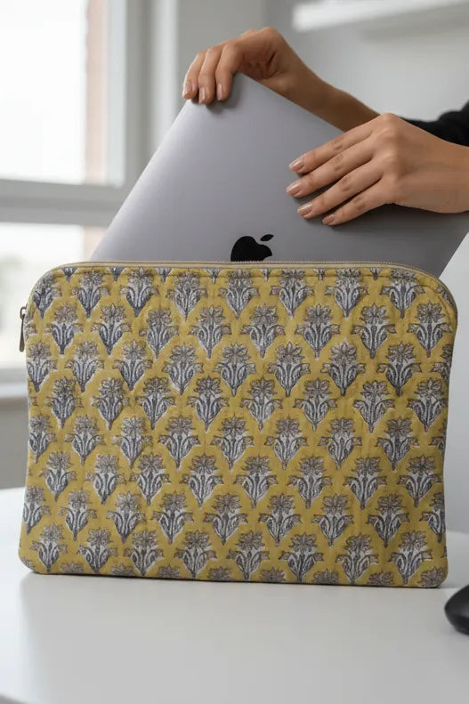Person holding a laptop with a yellow and gray patterned sleeve on a white surface.