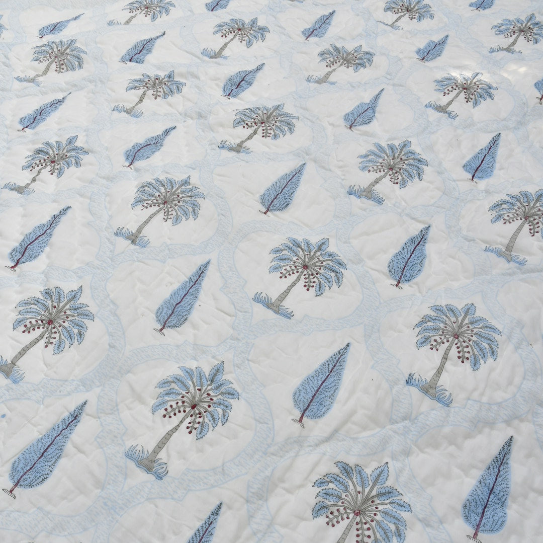 A close-up of a light blue and white quilted jaipuri design featuring embroidered palm trees and leaf motifs, with a braided border visible on the right.
