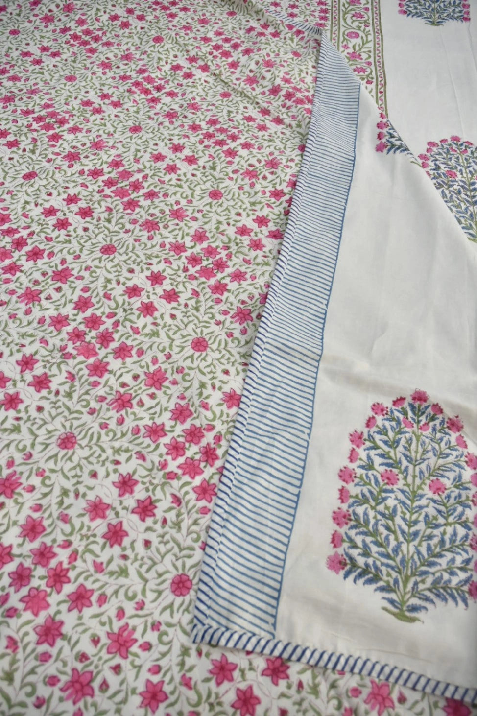A close-up of a white fdohar with an all-over pink floral print and a decorative border featuring blue stripes and a blue-and-pink tree motif.