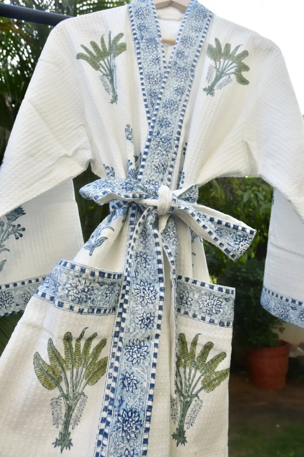 White kimono with blue and green patterns on a hanger against a blurred outdoor background