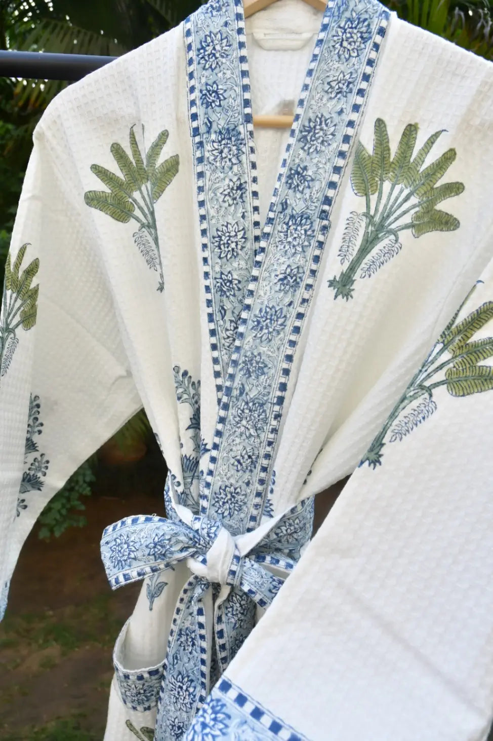 White kimono with blue floral patterns and green leaf designs on a blurred natural background