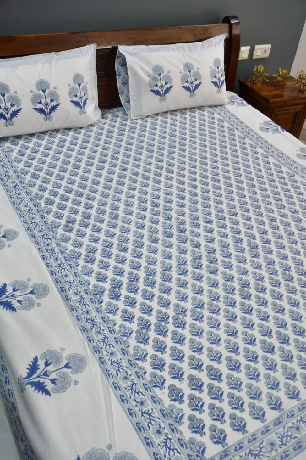 Bed with blue floral patterned bedding and pillows against a gray wall.