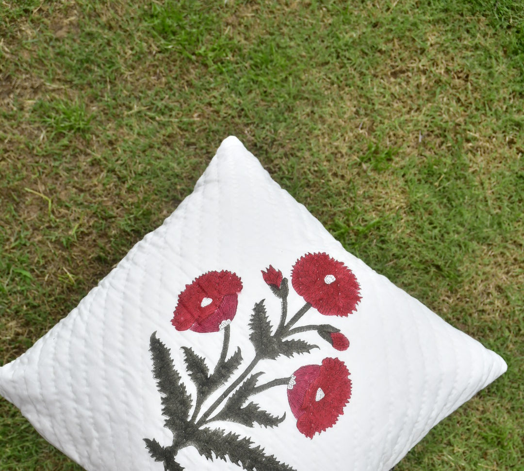 White pillow with red floral embroidery on a grassy background