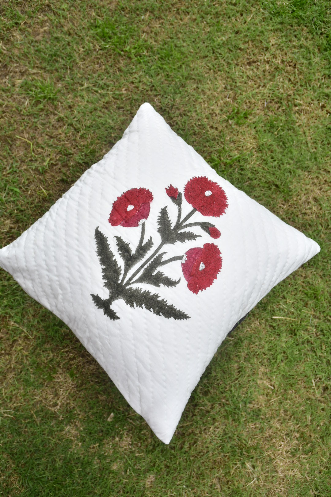 White pillow with red floral embroidery on a grassy background