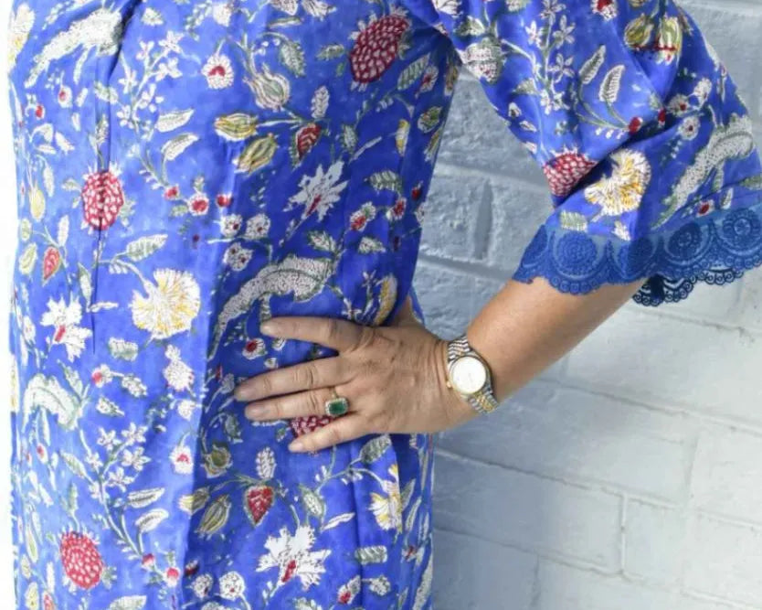 Woman wearing a blue floral dress against a white brick wall.