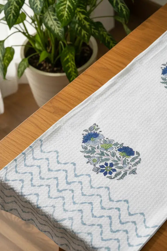 Cotton bath and towel set with floral design on a wooden table with plants in the background