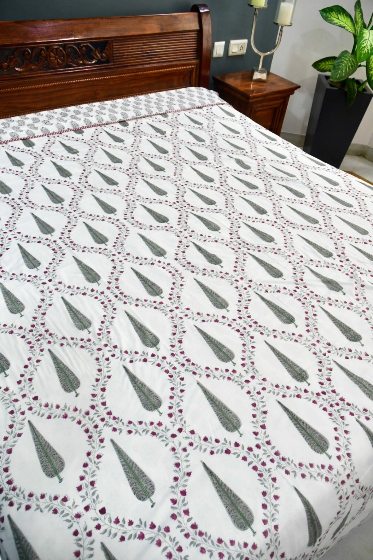 A white dohar with a repeating green and burgundy floral pattern, styled on a bed in a bedroom setting.