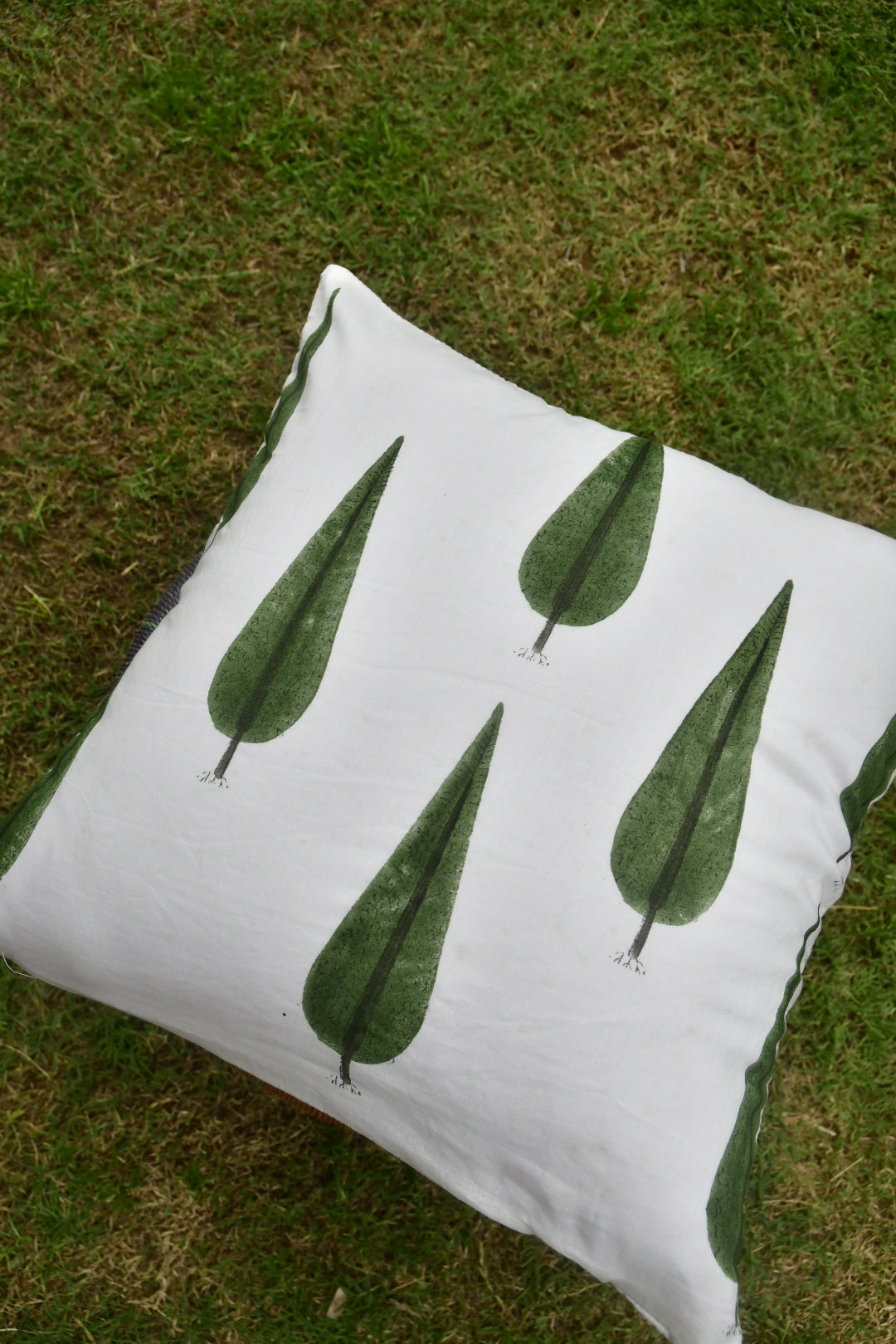 White pillow with green leaf patterns on a grassy background