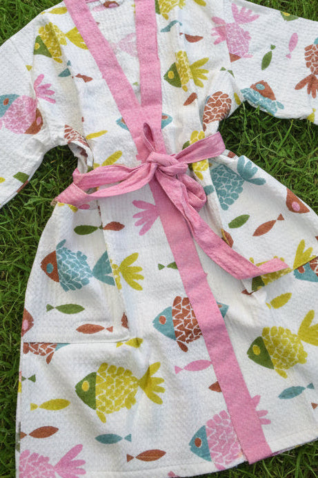 Children's robe with fish pattern and pink trim on grass