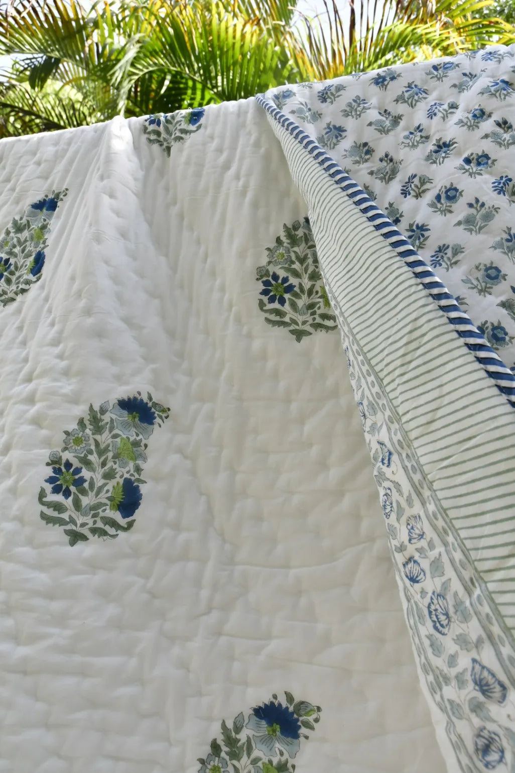 Floral-patterned quilt with green and blue designs on a white background