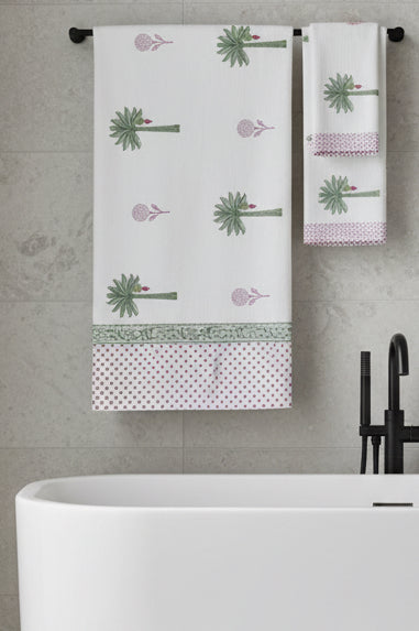 A white cotton tablecloth and matching napkins featuring a green palm tree print, pink polka dot borders, and a decorative green patterned band.