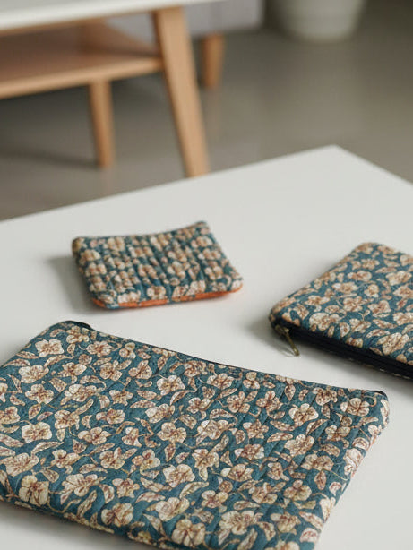 Three floral-patterned pouches on a textured surface with blue floral designs.