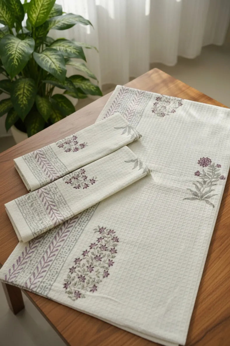 Set of embroidered table runner and napkins on a wooden table with a plant in the background.