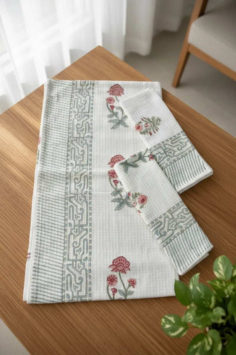 Set of patterned table runners on a wooden surface with a plant in the corner.