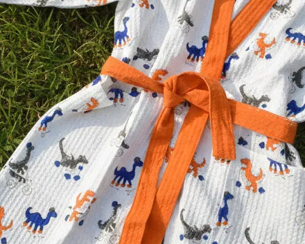 White robe with orange trim and dinosaur pattern on grass