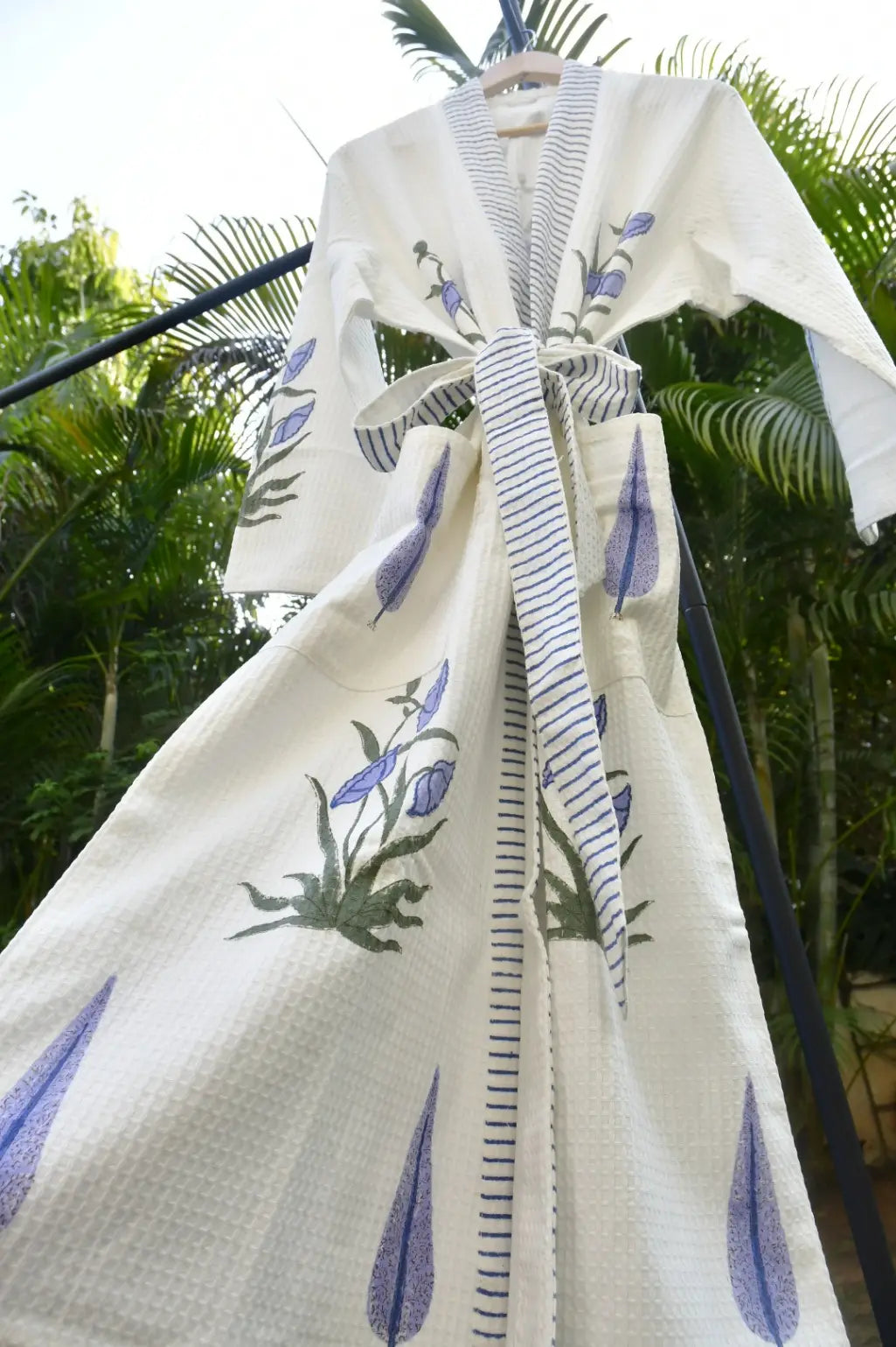 White garment with blue floral embroidery on a hanger against a green outdoor background