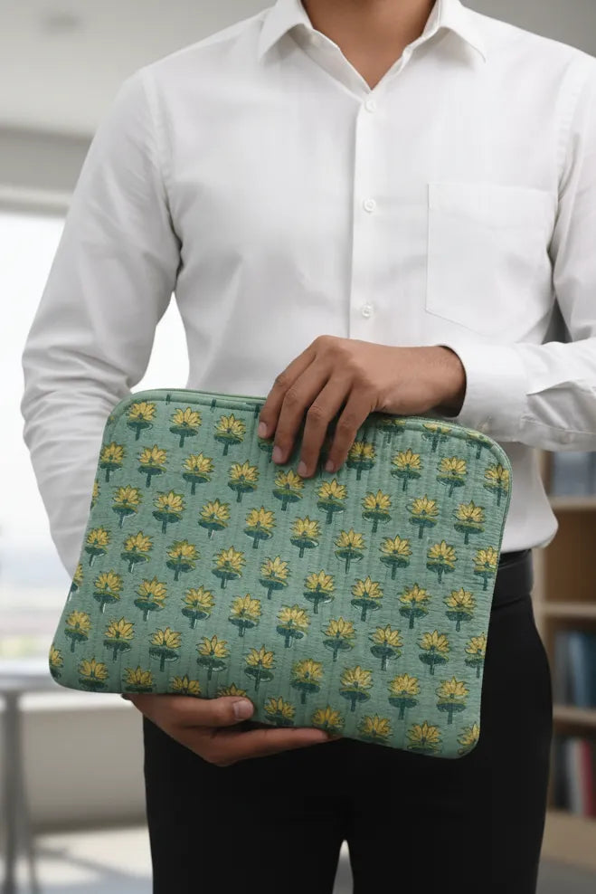 Person holding a green patterned laptop sleeve with a blurred indoor background