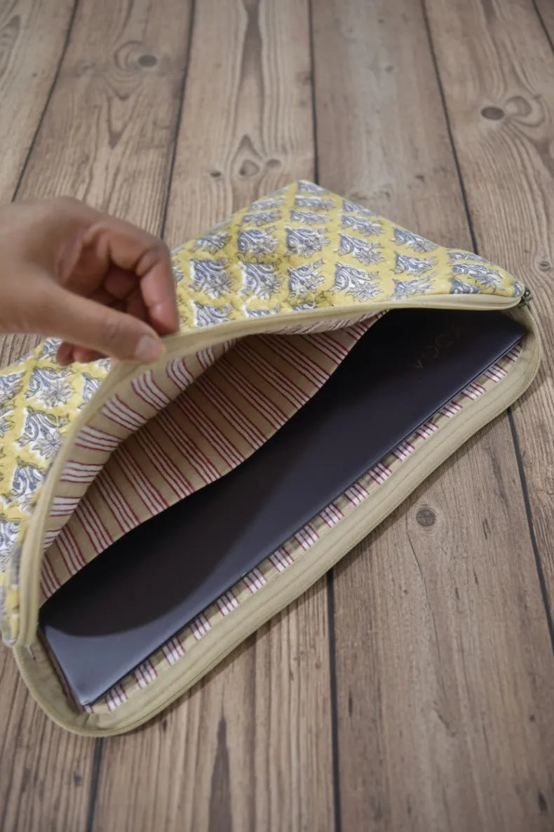 Hand holding a sleeve-wrapped laptop on a wooden surface
