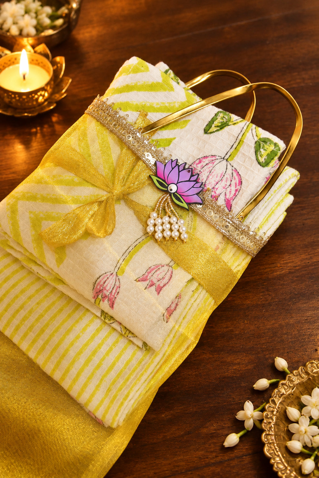 A folded yellow and white striped fabric item with a floral print, tied with a yellow ribbon and decorated with a small flower charm, resting on a dark wooden surface.
