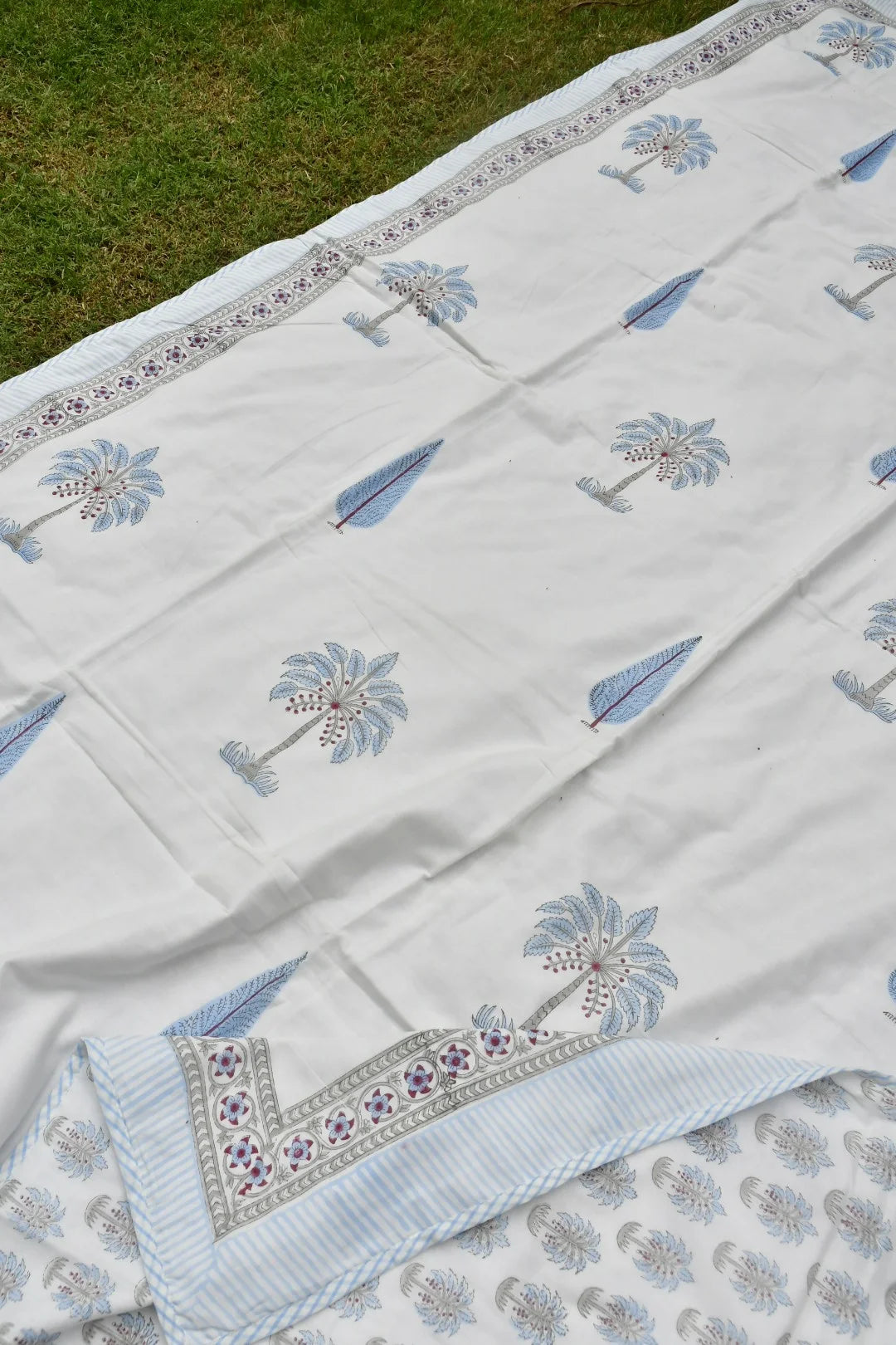 White embroidered fabric with blue floral patterns on a grassy background