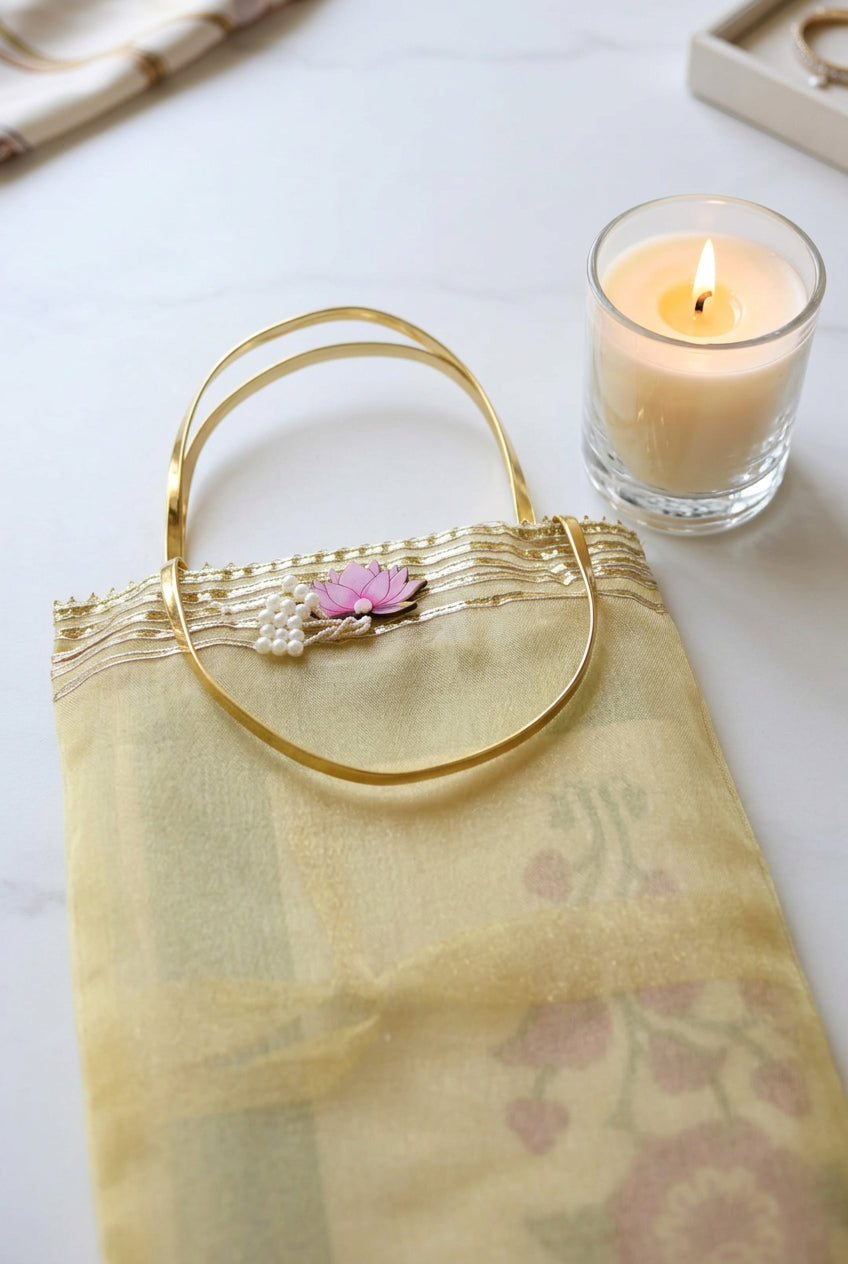 A pale yellow sheer organza handbag with a gold-tone metal handle, decorated with a small pink flower and white pearl embellishment at the top, resting on a dark wooden surface.