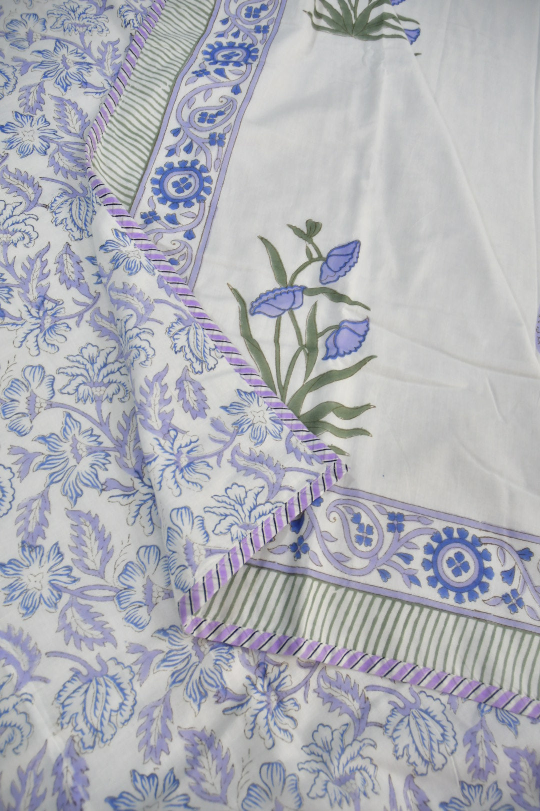 White cotton fabric with blue and purple floral block print, featuring a decorative border with blue floral motifs, green and white stripes, and purple stitched edges.
