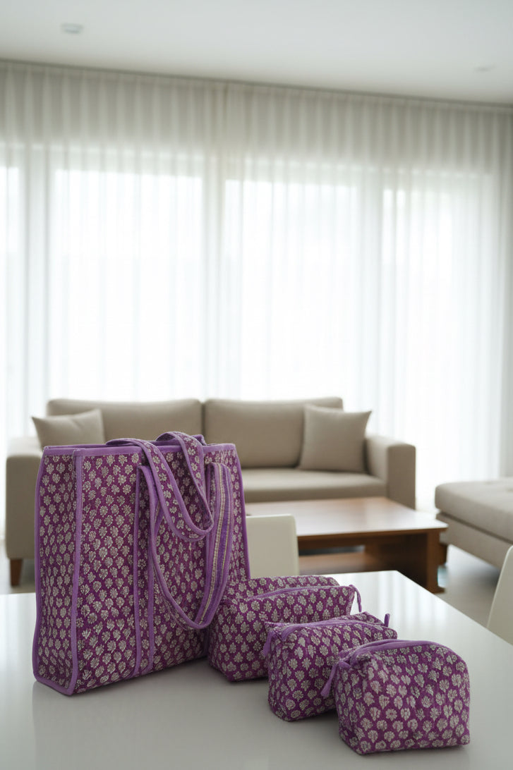 Purple patterned bags on a bed with floral bedding against a gray wall.