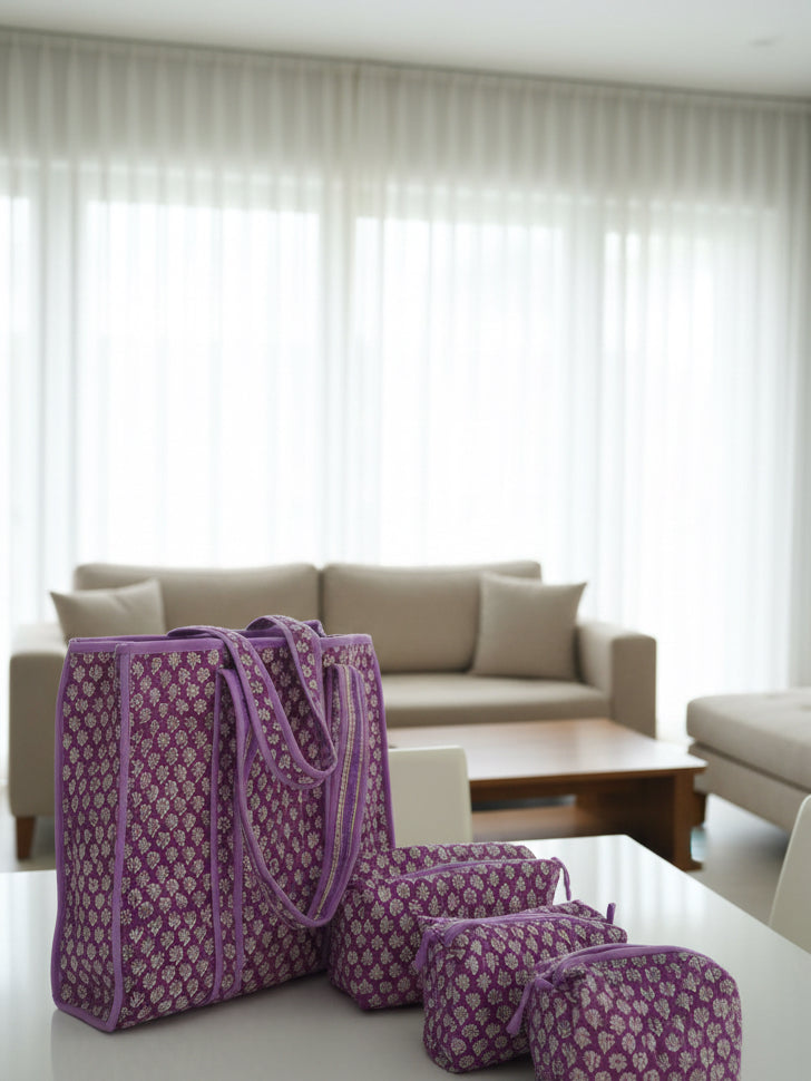 Purple patterned bags on a bed with floral bedding against a gray wall.