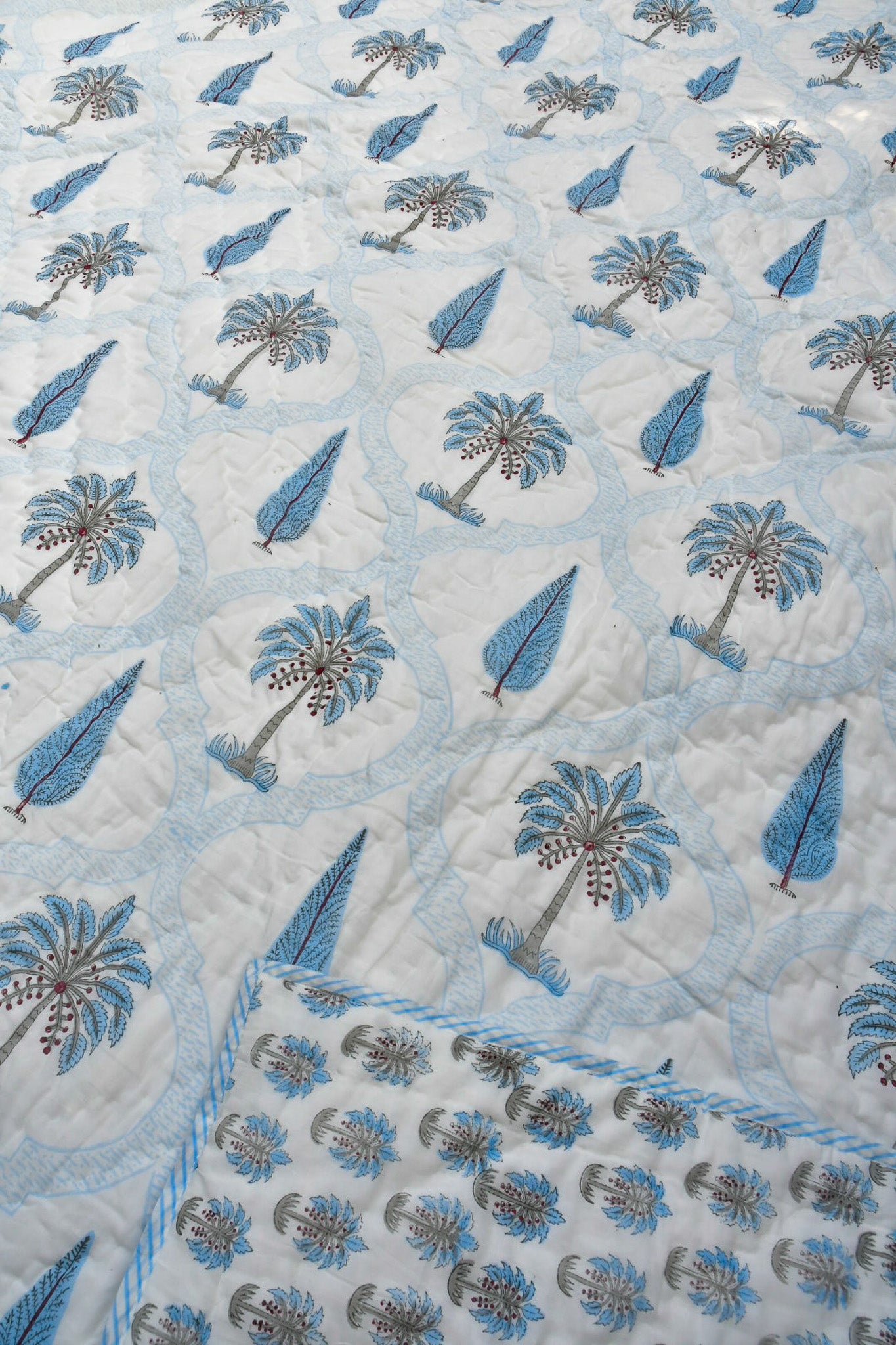 A close-up of a quilted jaipuri design featuring a repeating pattern of blue palm trees and blue teardrop motifs on a white background, with a matching blue and white border visible in the bottom corner.
