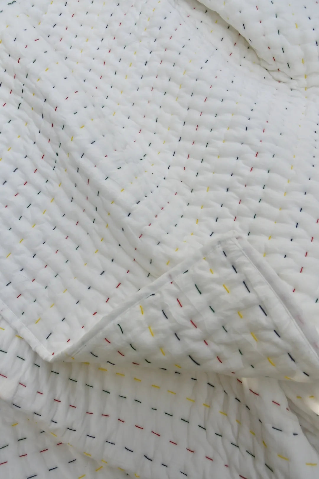 Close-up of a textured quilt with small colorful patterns on a white background