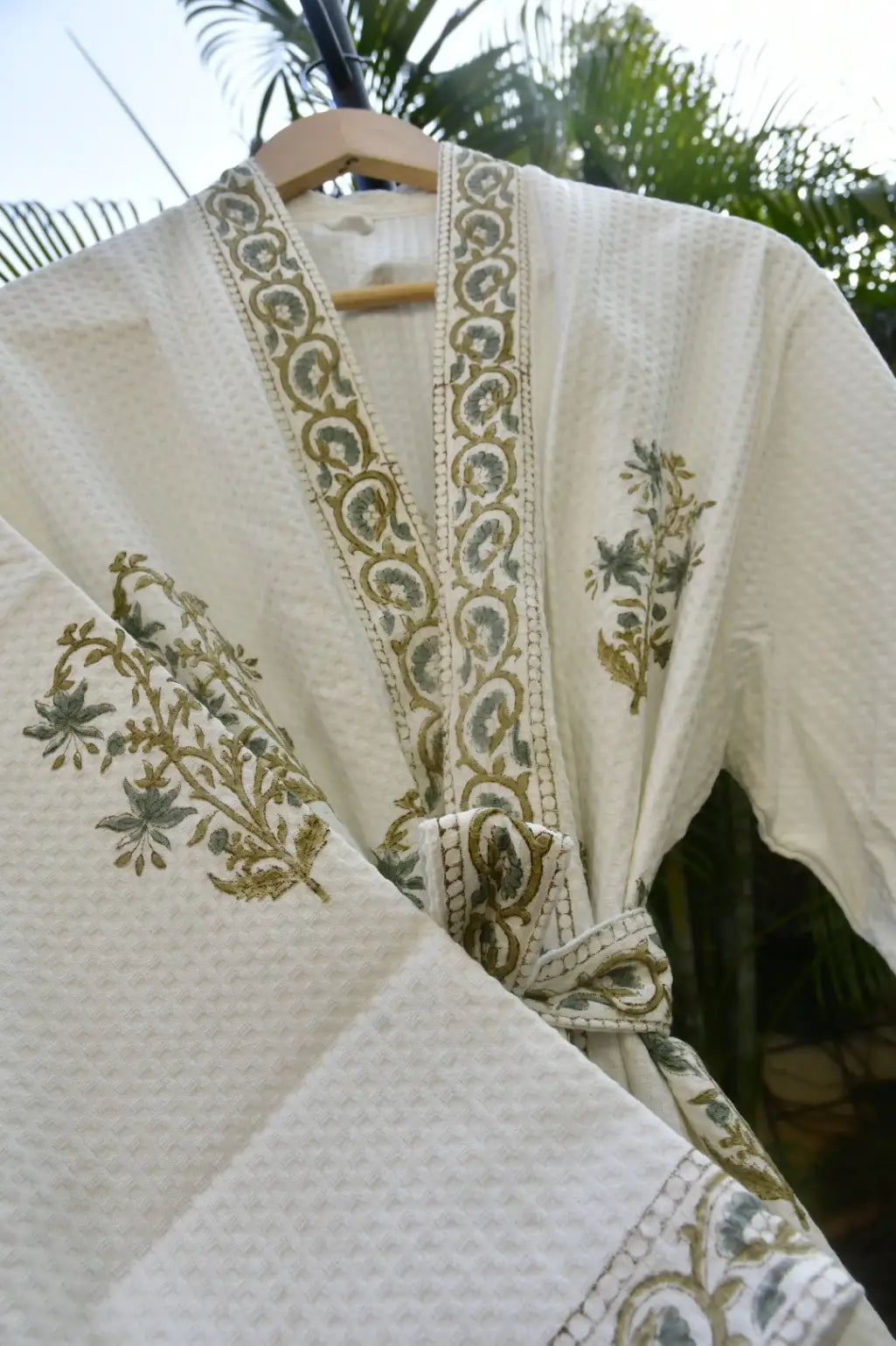 White embroidered garment on a hanger with greenery in the background