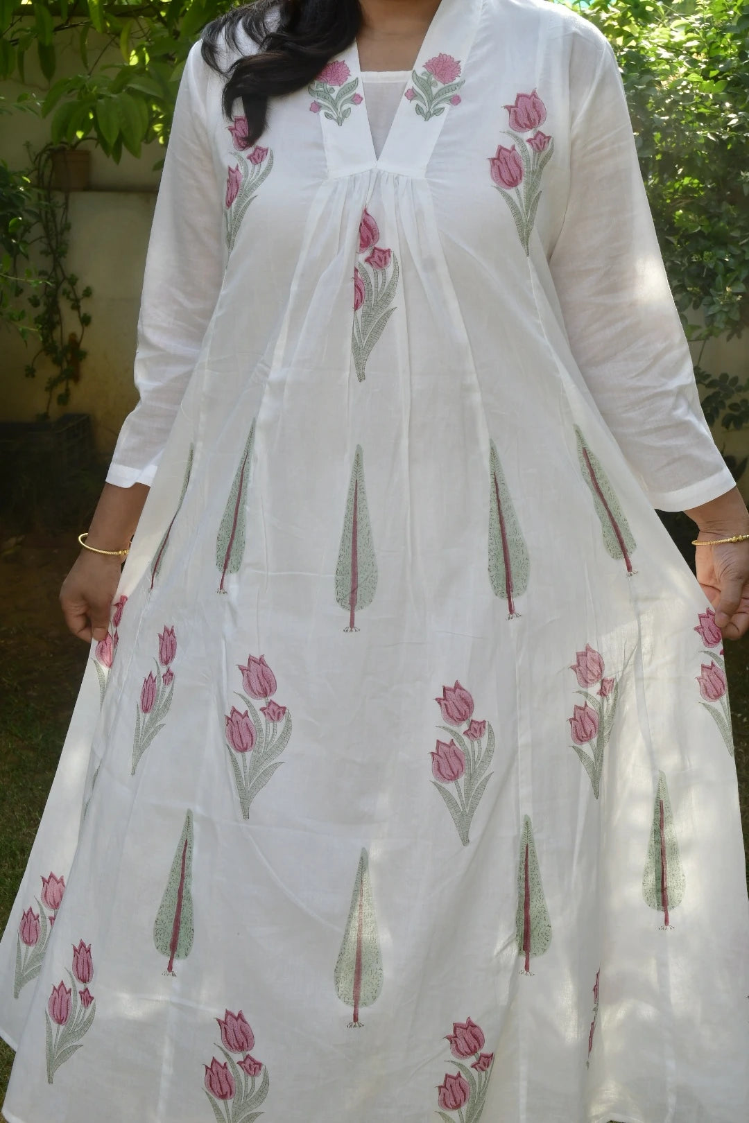 White dress with pink floral embroidery worn by a person outdoors.