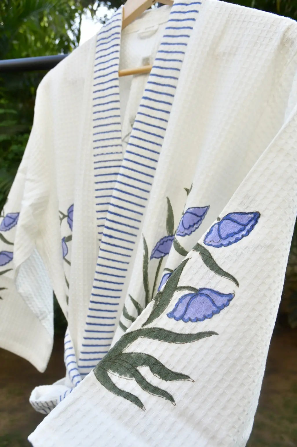 Blue and purple with blue floral embroidery on a hanger against a blurred natural background