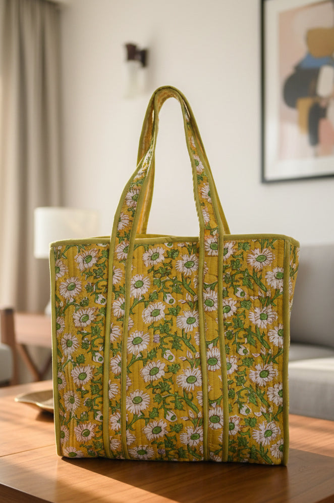 Yellow floral-patterned bag on a gray surface with a white cloth and colorful item in the background.