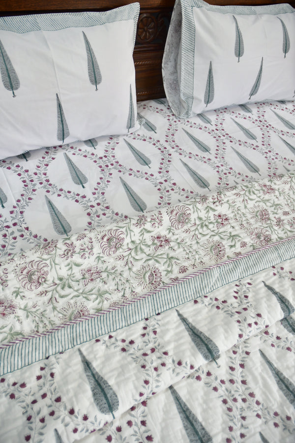 Floral quilt with feather patterned pillows on a wooden bed.