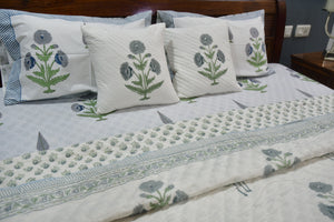 Floral-patterned bedspread and pillows on a bed in a bedroom setting.