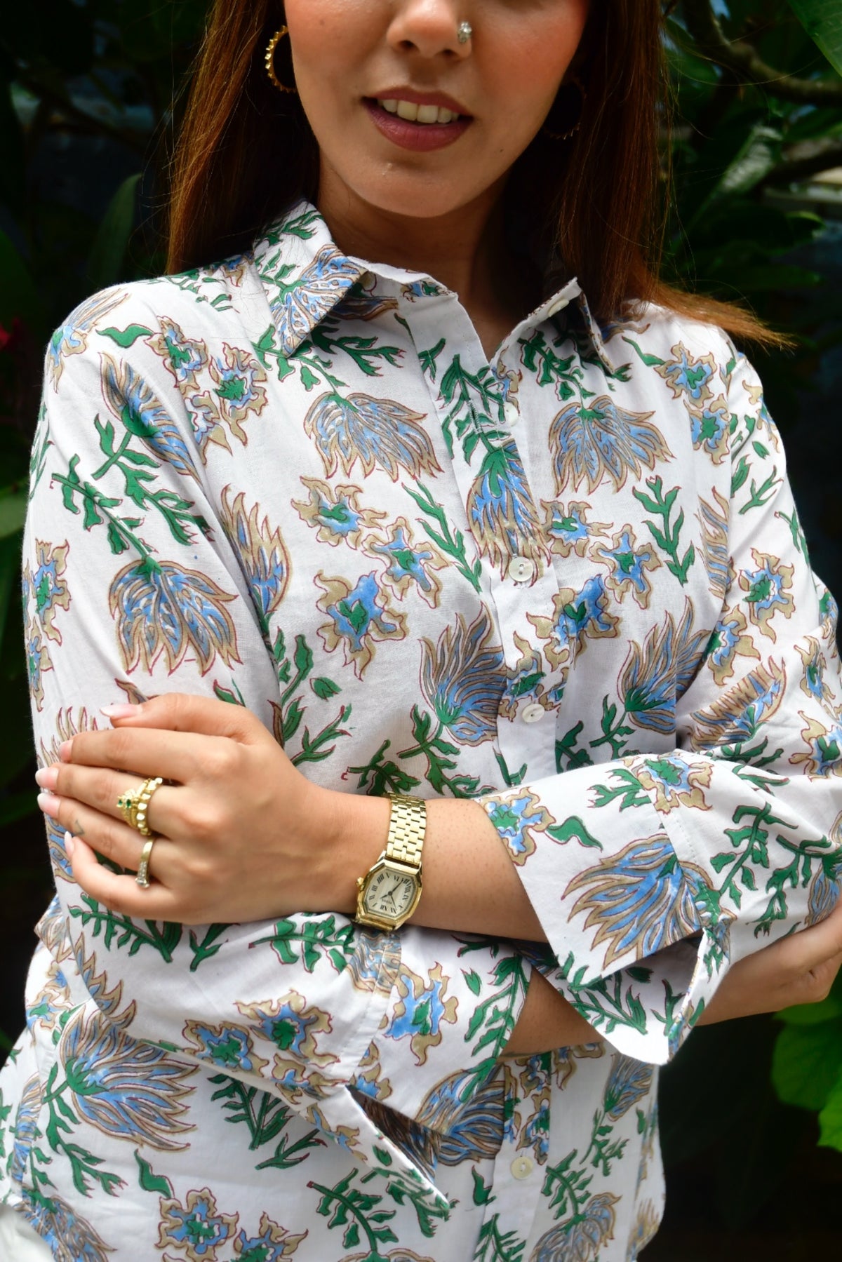 Woman wearing a white blouse with floral patterns, standing outdoors.