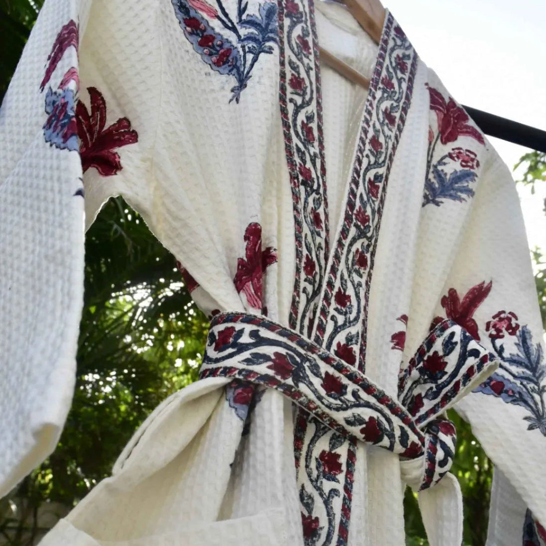 White bathrobe with red and blue floral patterns on a hanger against a blurred green background