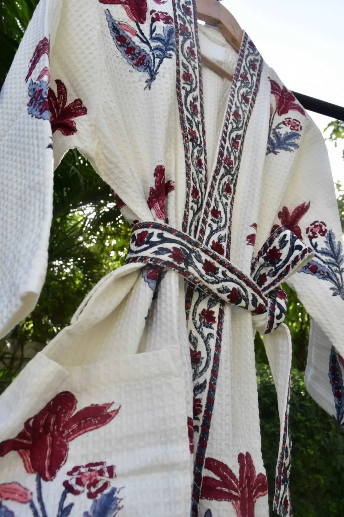 White fabric with red and blue floral patterns on a hanger against a blurred green background