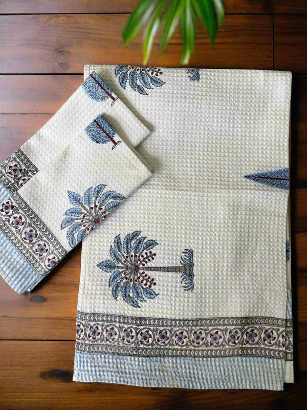 Set of two embroidered towels on a wooden surface with a plant in the background
