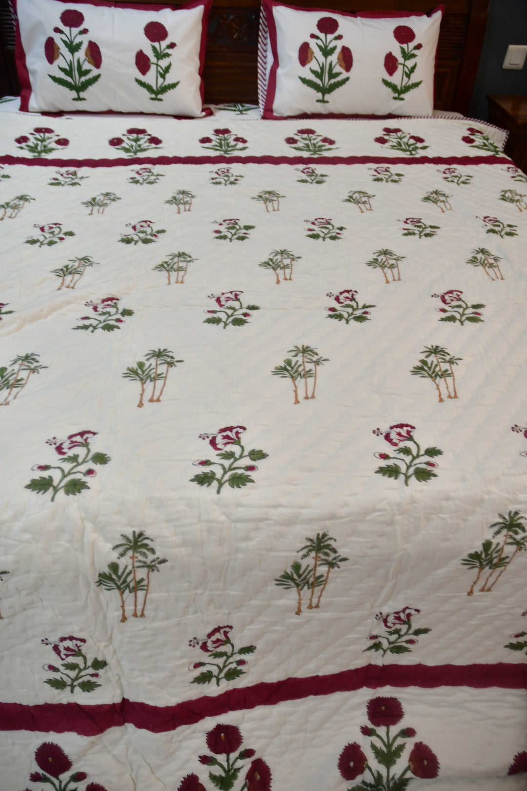 Bedspread with floral pattern and red border on a bed.