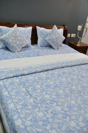 Bed with blue floral bedding and pillows against a gray wall.